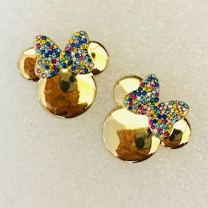 May include: A pair of gold-tone earrings with a Minnie Mouse design. The earrings feature a bow with colorful rhinestones.