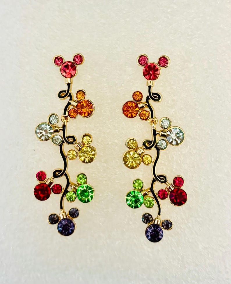 May include: A pair of dangle earrings with a Mickey Mouse head design. The earrings are made of gold-tone metal and feature a cascade of colorful crystals in a rainbow pattern.