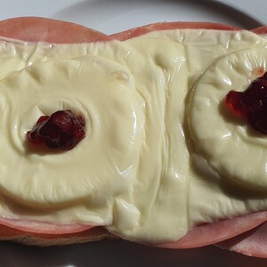 May include: A toasted bread sandwich with ham, cheese, and pineapple rings topped with red jelly.