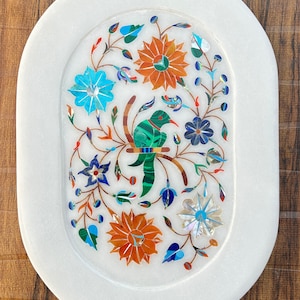 Puede incluir: Bandeja ovalada de mármol blanco con un diseño floral incrustado con piedras de colores. El diseño presenta un pájaro, flores y hojas.