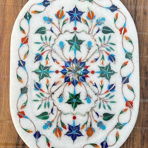 Puede incluir: Bandeja ovalada de mármol blanco con un diseño floral incrustado con piedras de colores. El diseño presenta flores azules, verdes, rojas y naranjas con detalles intrincados.