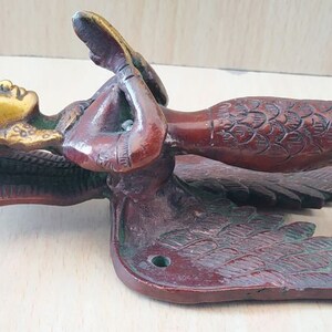 May include: A bronze-colored door handle featuring a mermaid design. The handle has a detailed mermaid figure with a golden face and flowing hair, wings, and a scaled tail. The handle is likely made of metal and has a vintage or antique aesthetic.
