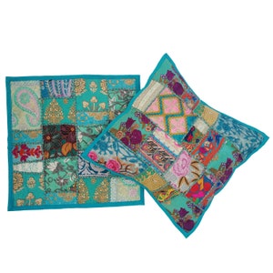 May include: Two turquoise blue patchwork cushion covers with colourful floral embroidery and sequins. The cushions are made from a variety of fabrics and have a bohemian style.