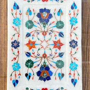 Puede incluir: Una bandeja de servir de mármol blanco con un intrincado diseño floral incrustado con piedras de colores. El diseño presenta flores azules, rojas, verdes y naranjas.