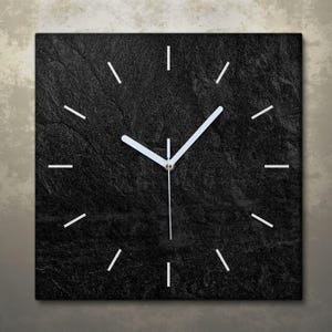 May include: Square wall clock with a textured black face. The clock features white hands and white linear hour markers. The clock's design is minimalist and modern, suitable for home or office decor.