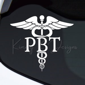 May include: White vinyl decal of a medical caduceus symbol with the letters PBT inside the snake. The decal is on a black car window.