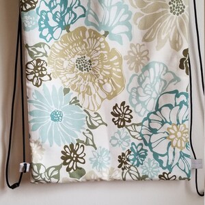May include: A white drawstring bag with a floral pattern in shades of blue, green, and brown. The bag has black drawstrings and a gray fabric lining.