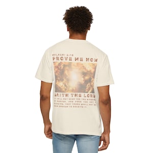 May include: Cream-colored t-shirt with a graphic on the back featuring the text "PROVE ME NOW" and "SAITH THE LORD" above a cloudy sky image. The shirt is a casual, short-sleeved style.