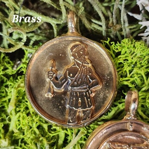 May include: Brass pendant featuring a detailed image of a man holding a staff. The pendant is round and has a raised edge. The man is depicted in a stylized, medieval-inspired design.