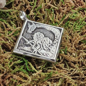 May include: A square, silver pendant featuring a detailed relief of a mythical figure with a dragon. The pendant has a loop at the top for a chain. The background is a bed of green and brown moss.