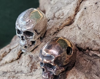 May include: Two silver skull beads with gold accents. The skulls are detailed and have a textured finish.
