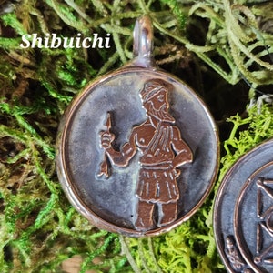 May include: A round, bronze-colored pendant with a raised image of a man holding a spear. The pendant has a loop at the top for attaching to a chain or cord. The image is in a dark, aged style.