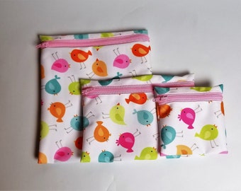 May include: Three zippered pouches with a white background and a colorful bird pattern. The pouches are different sizes and have pink zippers.