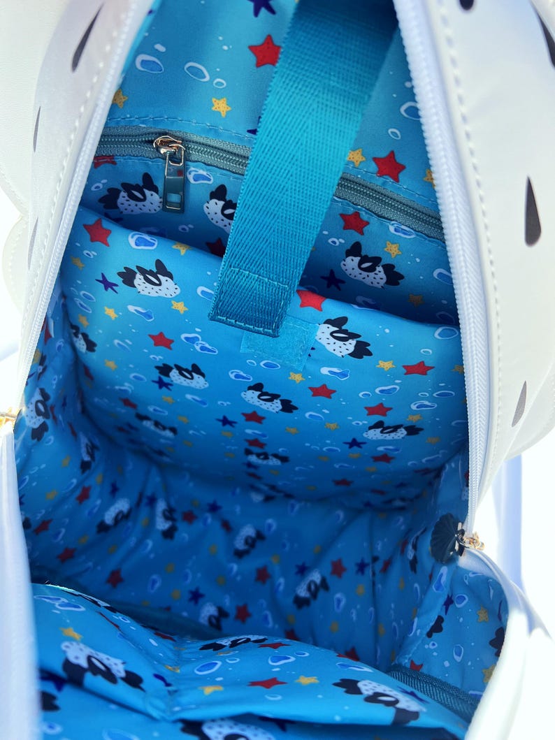 May include: The inside of a white pufferfish backpack with a blue lining. The lining has a pattern of pufferfish, stars, and bubbles. The backpack has a zippered pocket on the inside.