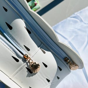 May include: White zippered bag with a seashell zipper pull. The bag has a black and white watermelon pattern.