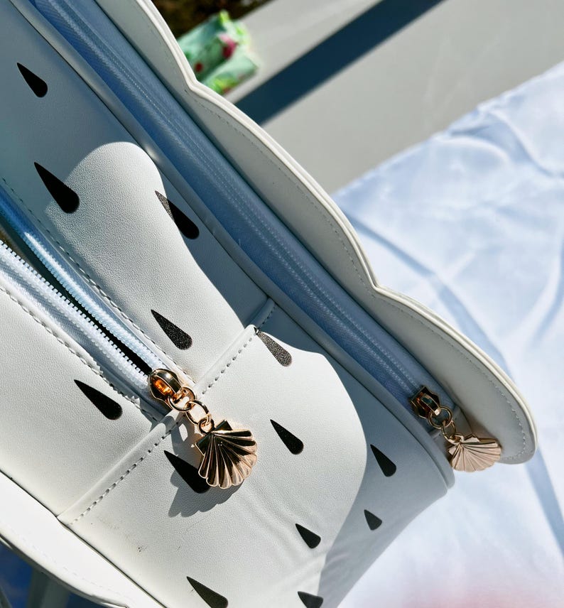 May include: White zippered bag with a seashell zipper pull. The bag has a black and white watermelon pattern.