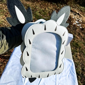 May include: White faux leather purse with black and white ears and black teardrop-shaped accents. The purse has a clear plastic window.