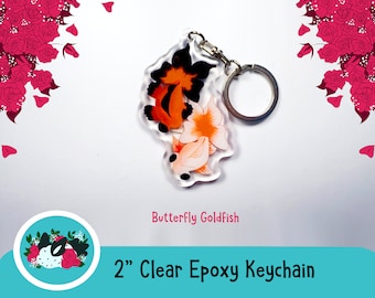 May include: A 2 inch clear epoxy keychain featuring a butterfly goldfish design. The goldfish is orange, white, and black. The keychain has a silver metal ring.