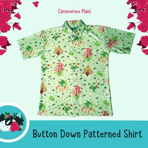 Può includere: Una camicia verde abbottonata con un motivo di piante carnivore rosa e verdi. La camicia ha un colletto e maniche corte. Il testo "Carnivorous Plant" è stampato sopra la camicia e "Button Down Patterned Shirt" è stampato sotto la camicia.