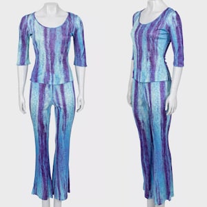May include: A two-piece outfit featuring a scoop-neck top with three-quarter sleeves and matching flared pants. The set is a blend of blue and purple vertical stripes. The outfit is displayed on a mannequin.