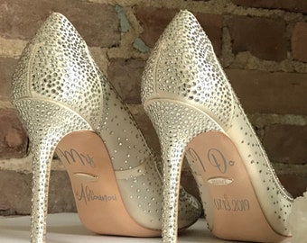 May include: A pair of white high-heeled shoes with rhinestones. The heels are decorated with the text "Mr. & Mrs." and "I Do" with the date "07.13.2019".