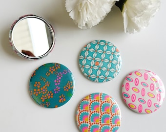 May include: Five round compact mirrors with different colorful patterns. The mirrors are teal, white, and pink with geometric and floral designs.