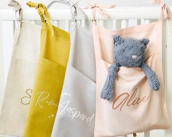 May include: Three hanging fabric storage bags with pockets. The bags are beige, yellow, and pink. The bags are personalized with the names "Sam", "Rom Gaspard", and "Alice".