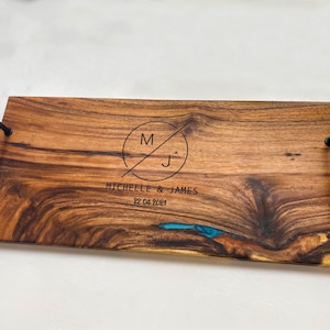 May include: A wooden serving tray with black metal handles. The tray is engraved with the initials "M" and "J" in a circle, along with the text "Michelle & James" and the date "22.04.2021".