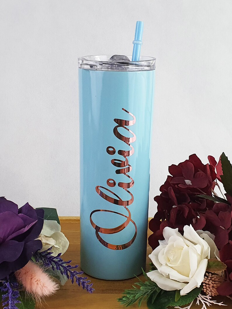 K&ouml;nnte beinhalten: Ein hellblauer Edelstahlbecher mit einem ros&eacute;goldenen Deckel und Strohhalm. Der Becher tr&auml;gt den Namen "Olivia" in ros&eacute;goldenen Lettern.
