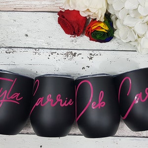Puede incluir: Cuatro vasos de vino de acero inoxidable negro con letras rosas. Los vasos est&aacute;n personalizados con los nombres Tayla, Carrie, Deb y Carla.