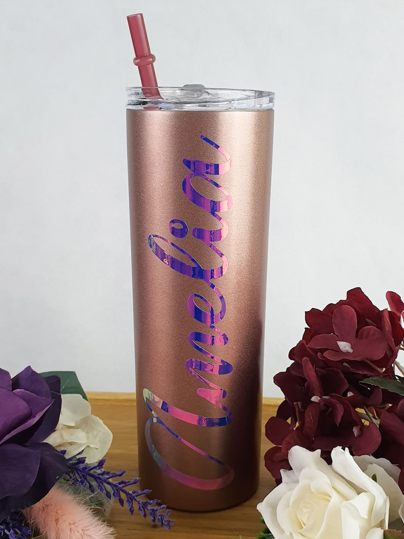 K&ouml;nnte beinhalten: Ein ros&eacute;goldener Edelstahlbecher mit einem regenbogenfarbenen Vinyl-Aufkleber, auf dem "Amelia" steht. Der Becher hat einen durchsichtigen Deckel und einen rosa Strohhalm.