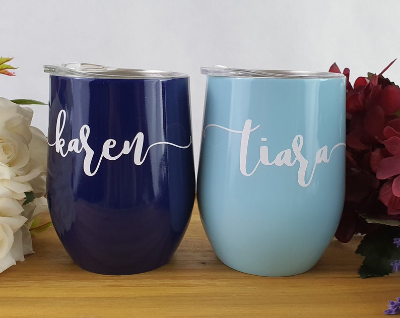 Puede incluir: Dos vasos de vino de acero inoxidable con tapas. El vaso de la izquierda es azul marino con el nombre "karen" escrito en blanco. El vaso de la derecha es azul claro con el nombre "tiara" escrito en blanco.