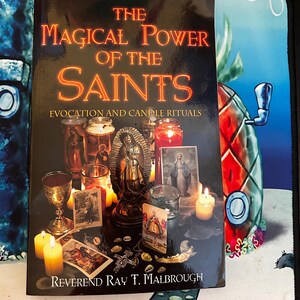 May include: A book titled "The Magical Power of the Saints" with the subtitle "Evocation and Candle Rituals." The cover features candles, religious statues, and images. The author's name, Reverend Ray T. Malbrough, is at the bottom.