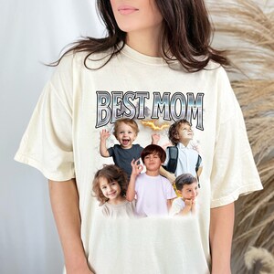 K&ouml;nnte beinhalten: Ein cremefarbenes T-Shirt mit dem Text "BEST MOM" in Silber und Schwarz gedruckt. Das Shirt zeigt eine Collage von Fotos von Kindern.