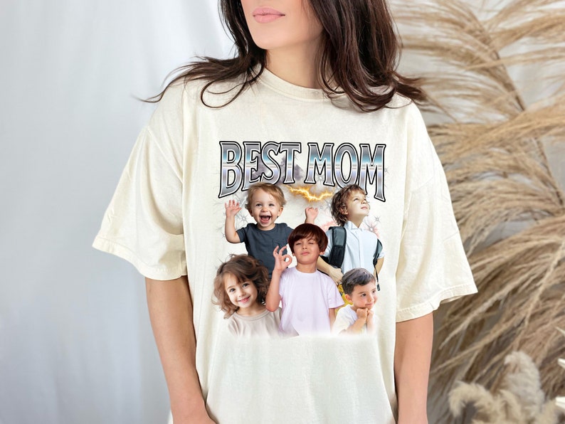 K&ouml;nnte beinhalten: Ein cremefarbenes T-Shirt mit dem Text "BEST MOM" in Silber und Schwarz gedruckt. Das Shirt zeigt eine Collage von Fotos von Kindern.