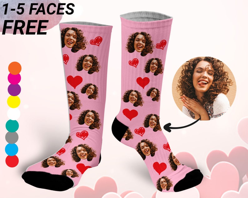 May include: A pair of pink socks with a heart pattern and multiple faces printed on them. The socks are knee-high and have a black toe and heel. The text "1-5 FACES FREE" is visible in the top left corner of the image.
