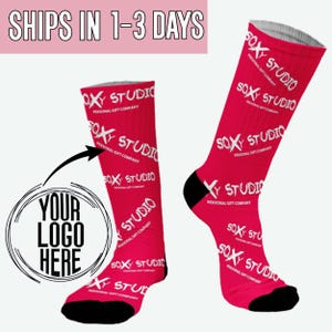 May include: A pair of pink socks with a white "SOXY STUDIO" logo repeated on the fabric. The socks have a black toe and heel. A white circle with the text "YOUR LOGO HERE" is in the image.
