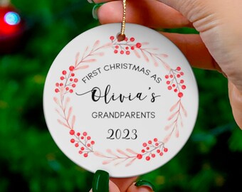 Peut inclure: Ornement de Noël en céramique blanche avec une couronne aquarelle rouge et rose et le texte "Premier Noël en tant que grands-parents d'Olivia 2023".