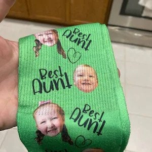 May include: Green socks with a repeated pattern of a child's face and the text "Best Aunt" with a heart.