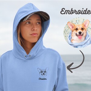 Peut inclure: Un sweat &agrave; capuche bleu clair avec une image brod&eacute;e en noir et blanc d'un chien avec le nom "Chester" en dessous. Le sweat &agrave; capuche a une capuche avec cordon de serrage et une poche kangourou.