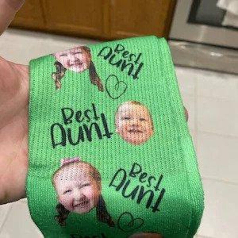 May include: Green socks with a repeated pattern of a child's face and the text "Best Aunt" with a heart.