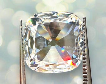 May include: A clear, faceted, cushion-shaped gemstone held in tweezers. The gemstone has a rainbow-like iridescence.