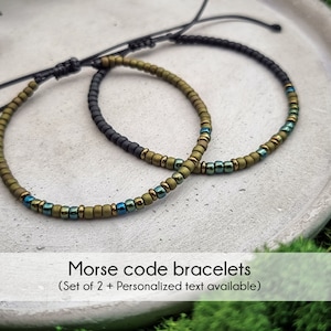 Könnte beinhalten: Zwei grüne und blaue Perlenarmbänder mit schwarzen Kordelbändern. Die Armbänder liegen auf einer weißen Oberfläche. Morsecode-Armbänder (Set mit 2 + Personalisierter Text verfügbar)