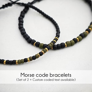 Könnte beinhalten: Zwei schwarze und grüne Perlenarmbänder mit goldenen Akzenten. Die Armbänder sind mit einer schwarzen Schnur zusammengebunden. Der Text "Morsecode-Armbänder (Set mit 2 + Benutzerdefinierter codierter Text verfügbar)" befindet sich unter den Armbändern.