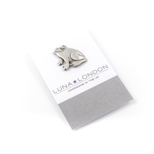 May include: A silver pewter frog pin on a white card with the text "LUNA★LONDON HANDMADE IN THE UK"