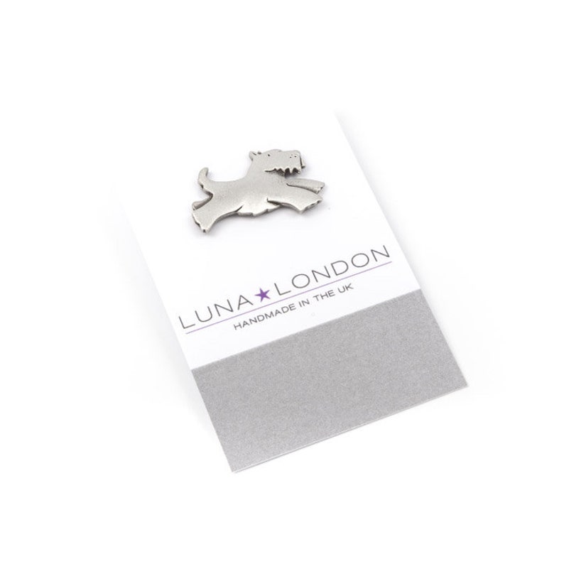 May include: A silver metal pin shaped like a Scottish Terrier dog. The pin is on a white card with the text "LUNA★LONDON HANDMADE IN THE UK".