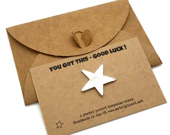 May include: A brown paper envelope with a heart-shaped closure. The envelope contains a card with the text "YOU GOT THIS - GOOD LUCK!" and a silver star-shaped pewter keepsake token. The card also includes the text "A pewter pocket keepsake token Handmade in the UK www.metalplanet.net"