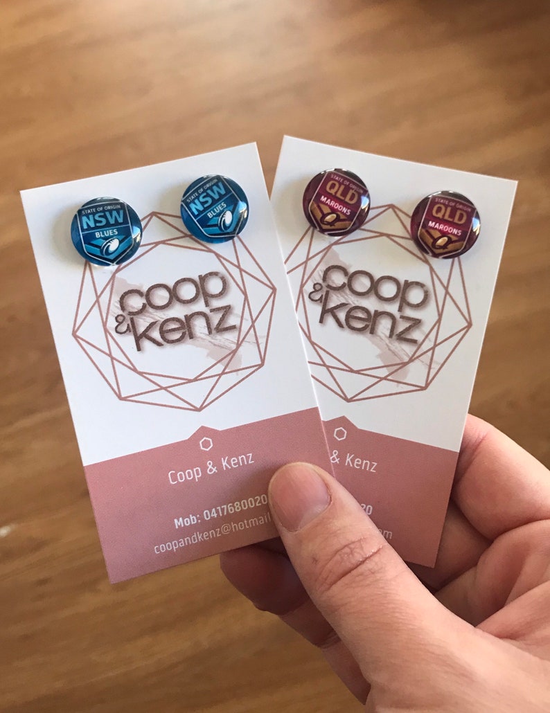 May include: Two business cards with a geometric design and the text "Coop & Kenz" printed on them. The cards are held in a hand. The text on the cards also includes a phone number and email address.