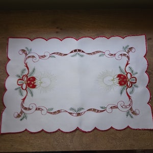 May include: White embroidered table runner with a scalloped edge. The embroidery features a red and green Christmas design with a ribbon and a bow.