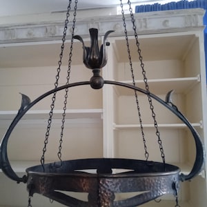 Könnte beinhalten: Ein antiker, hängender Metall-Kronleuchter mit dunkler Bronzefinish. Der Kronleuchter hat ein kreisförmiges Design mit dekorativen Haken und ist an Ketten aufgehängt. Die Leuchte hat ein zentrales blütenförmiges Element und gebogene Arme.